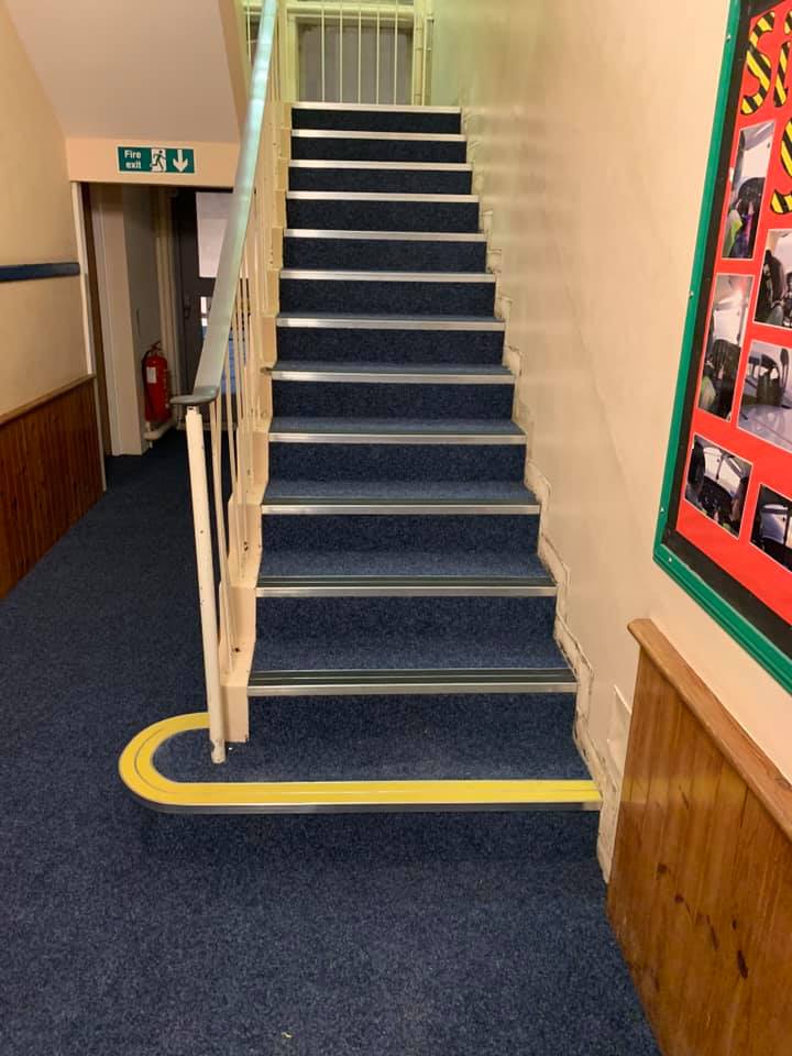 A staircase in a hallway with a stairlift rail that oddly ends at the wall below the stairs, making it unusable for access to the steps.
