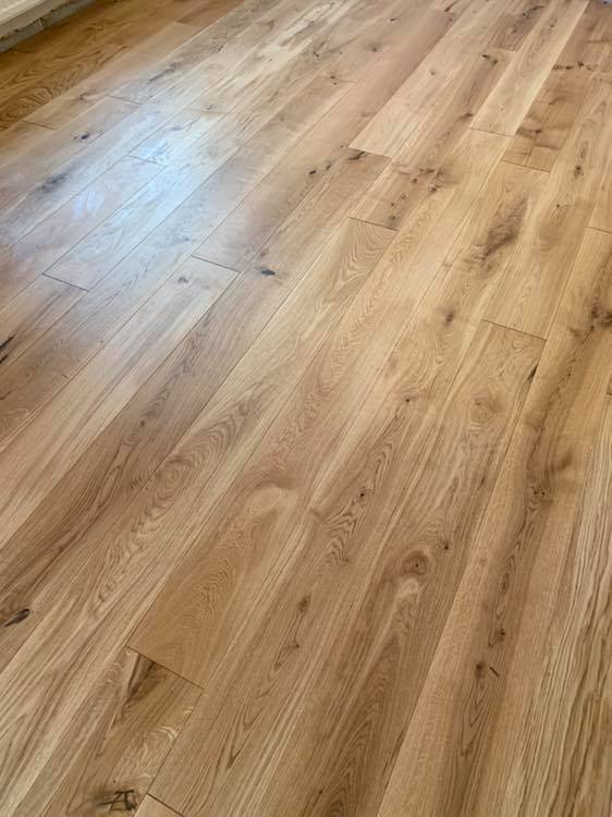Close-up view of a wooden floor with light brown planks, featuring natural wood grain patterns and knots. The planks are neatly arranged, creating a smooth and clean surface.