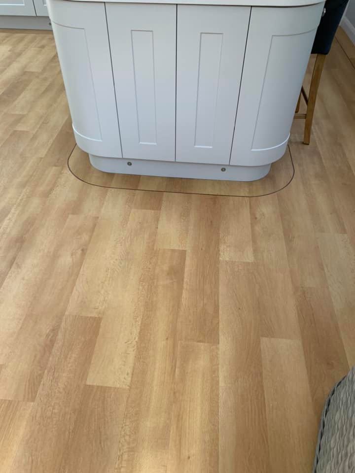 A kitchen island with white cabinets stands on a light wood floor. A faint curved outline is visible around the base of the island, indicating a possible moveable or liftable section of the floor.
